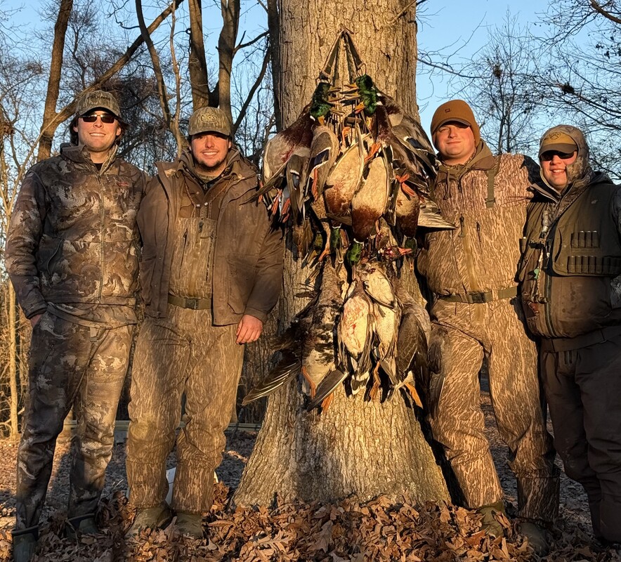 A group of young men posing around their haul after a duck hunt. 