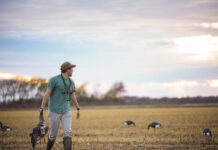 Generation Next A young man carrying a dead duck by the neck walks through a plain decorated with decoys.